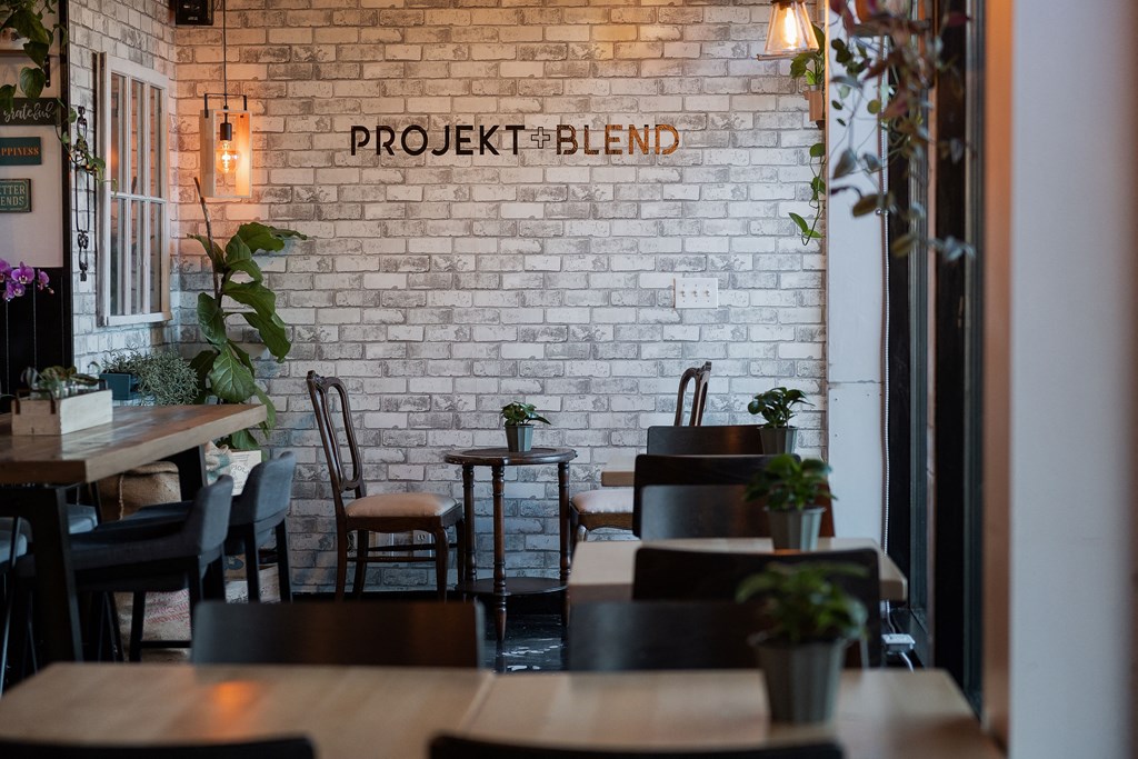 A restaurant with tables and chairs in front of a white brick wall with the word "PROJEKT" written on it.