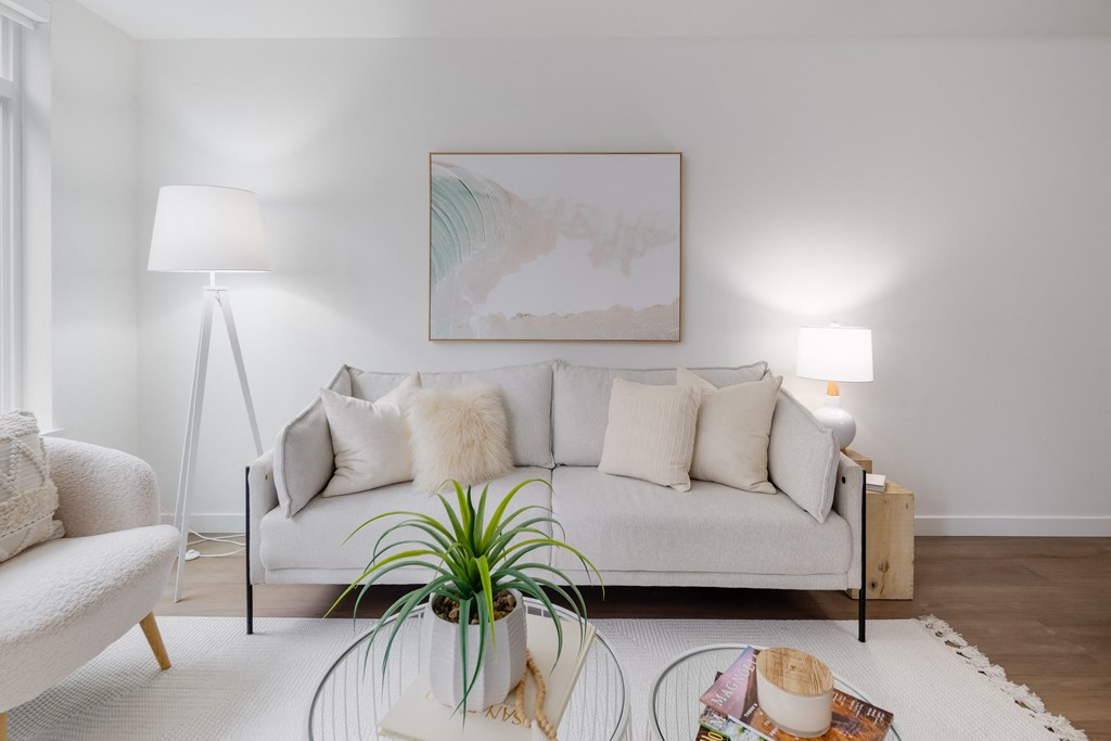 A living room with a white couch, a plant, and a painting on the wall.