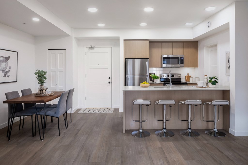 A modern kitchen with a dining table and bar stools.