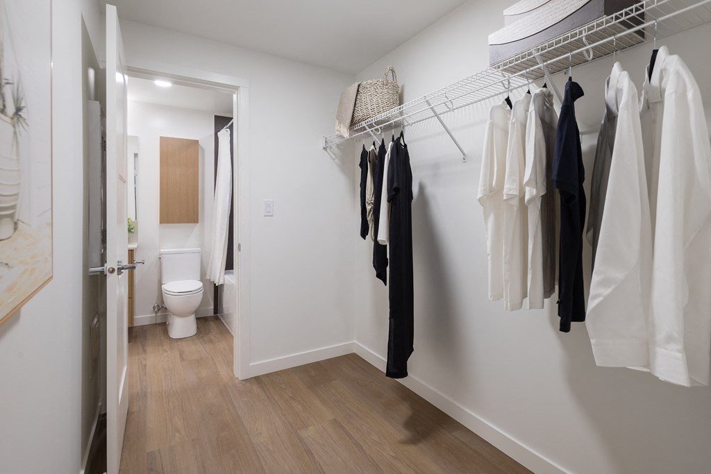 A hallway with a toilet and clothes hanging up.