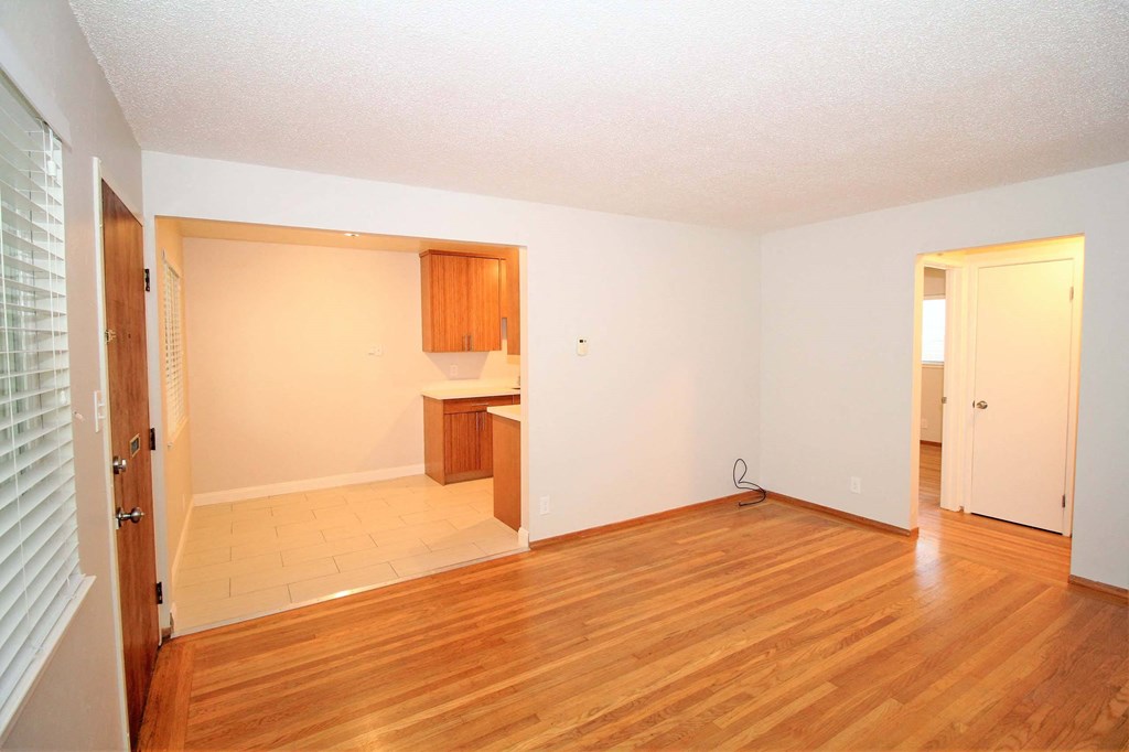 an empty living room with wood floors and a kitchen