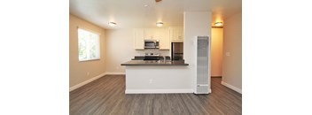 an empty living room with a kitchen with a refrigerator and a microwave