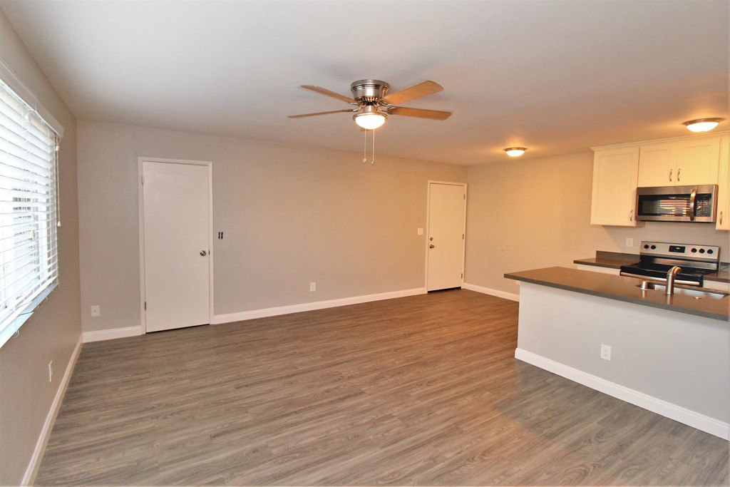an empty living room with a kitchen and a ceiling fan