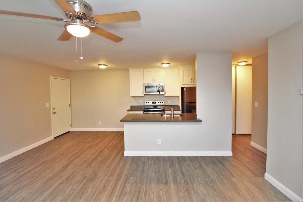 an empty living room with a kitchen and a ceiling fan