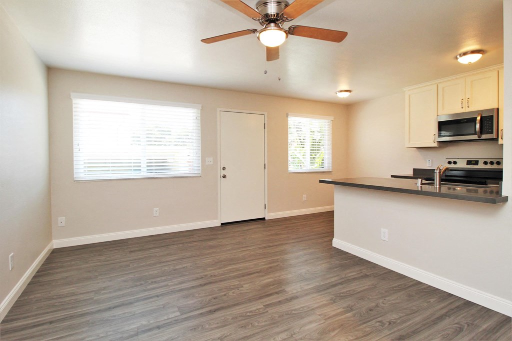 an empty living room with a kitchen and a ceiling fan