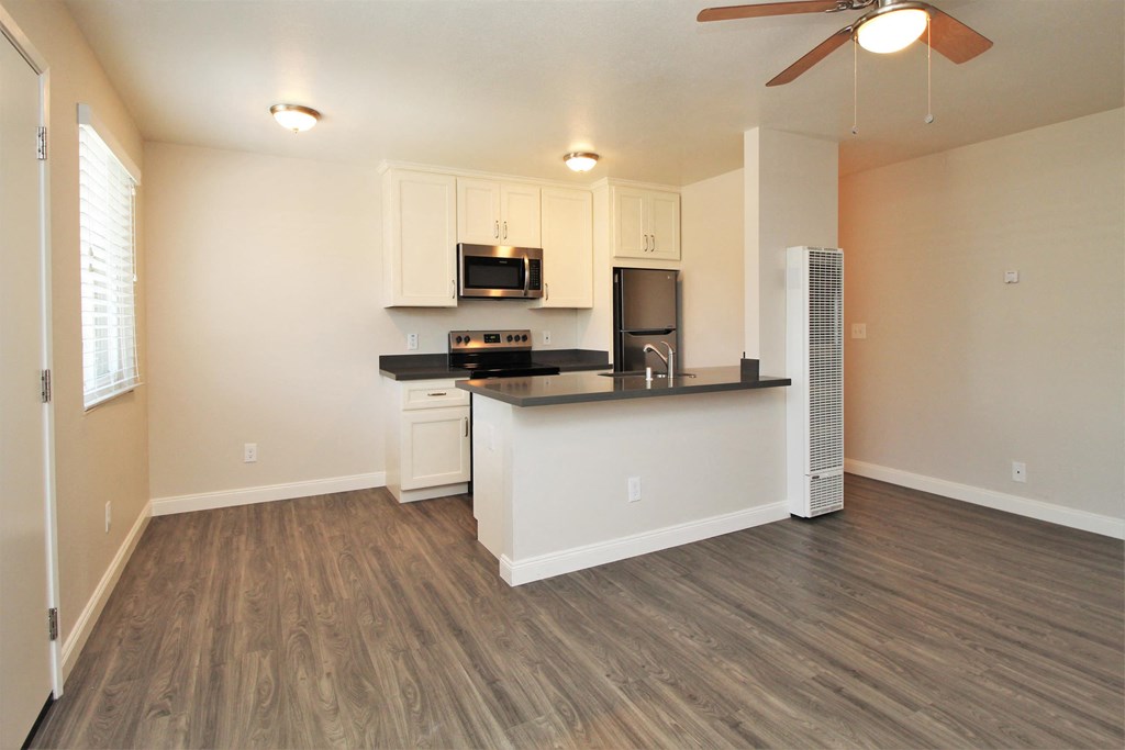 an empty living room with a kitchen and a ceiling fan