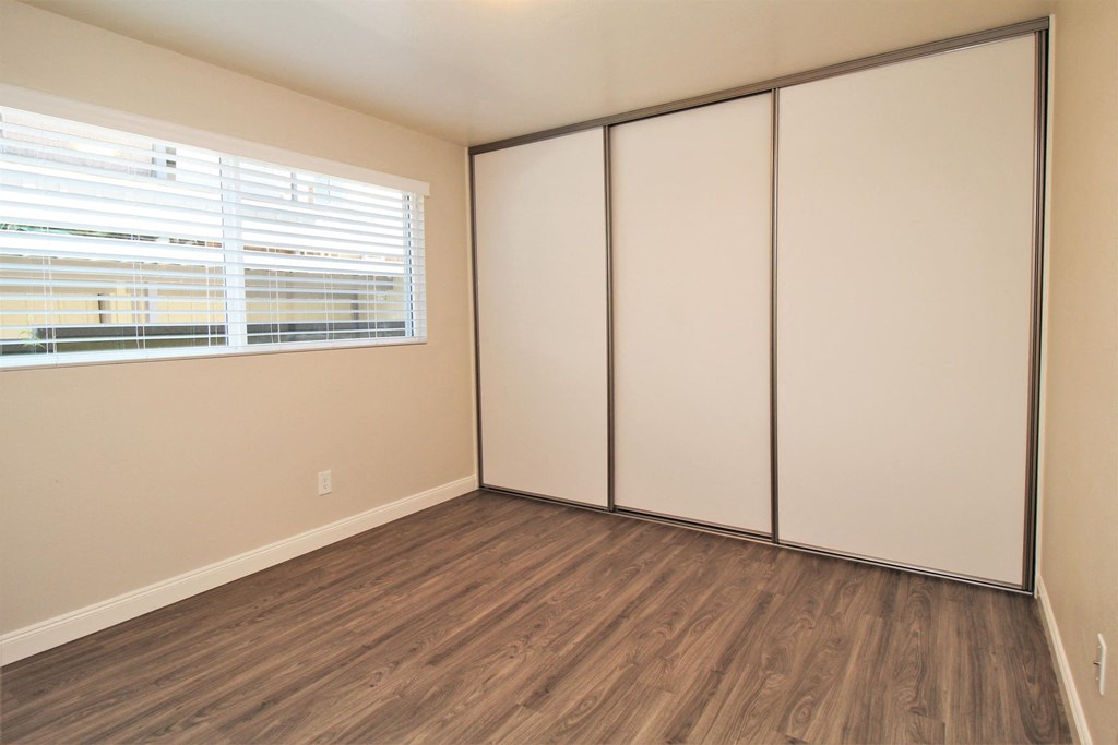 a bedroom with white walls and wood flooring and a window
