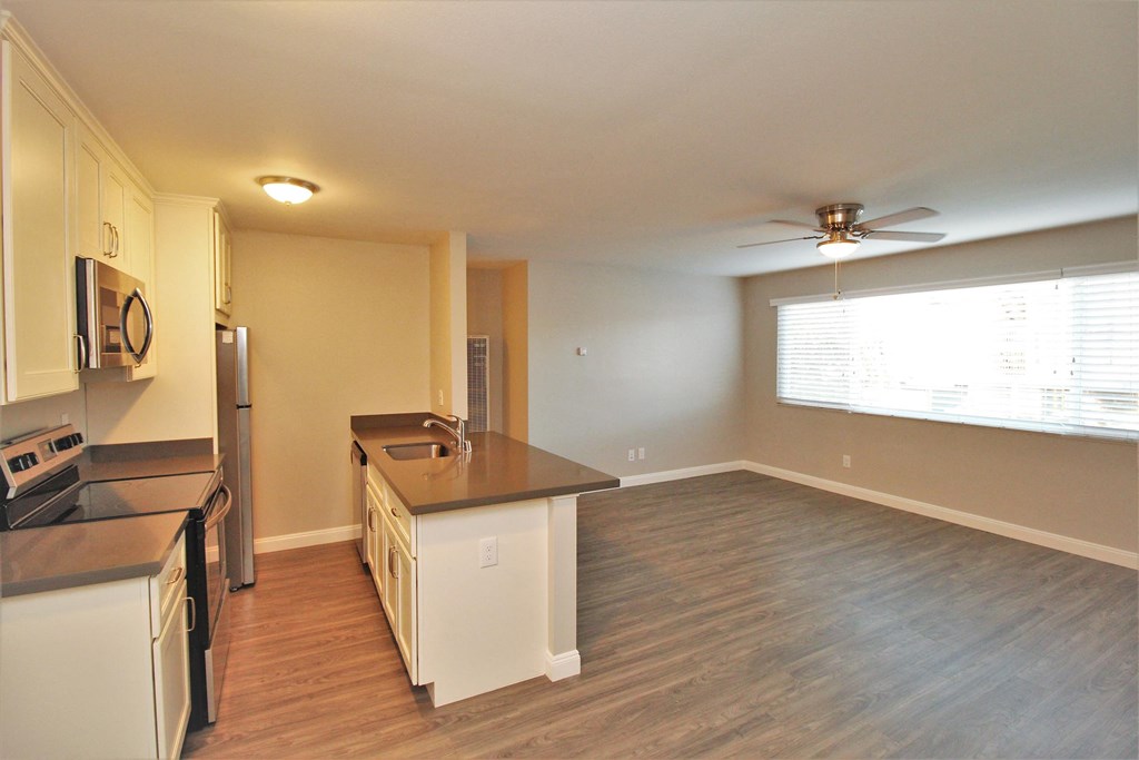 an empty living room with a kitchen and a ceiling fan