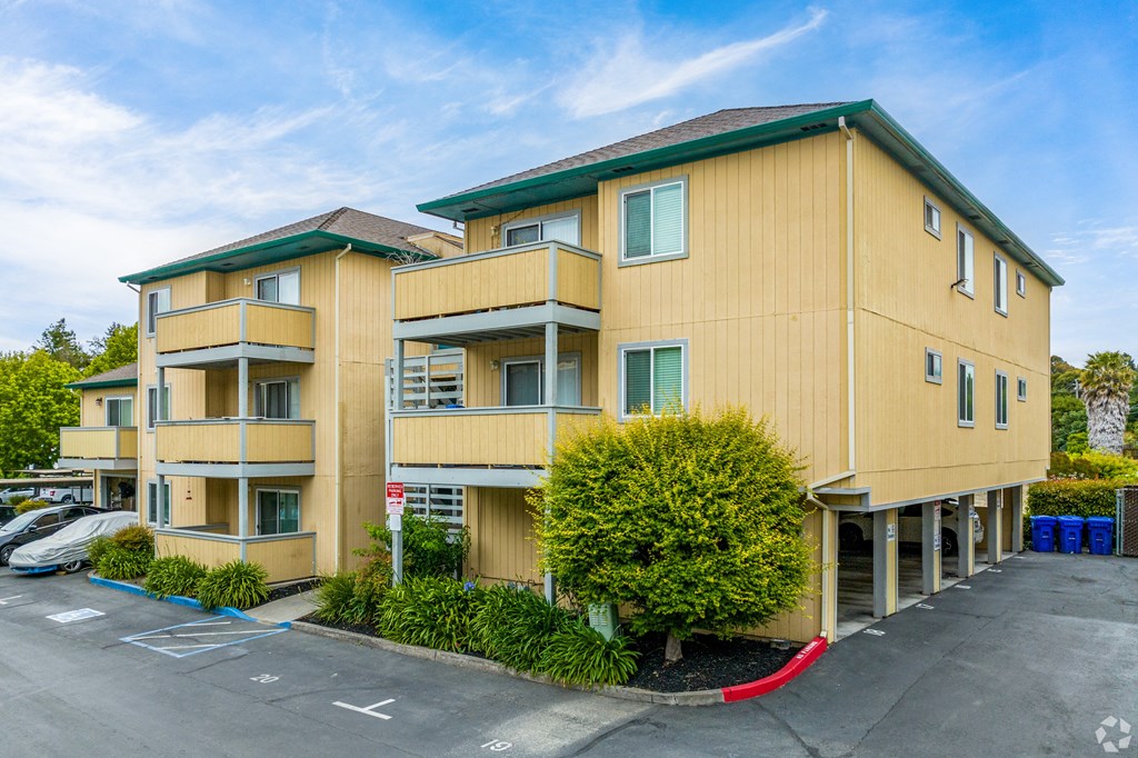 a yellow apartment building with a parking lot and a red curb