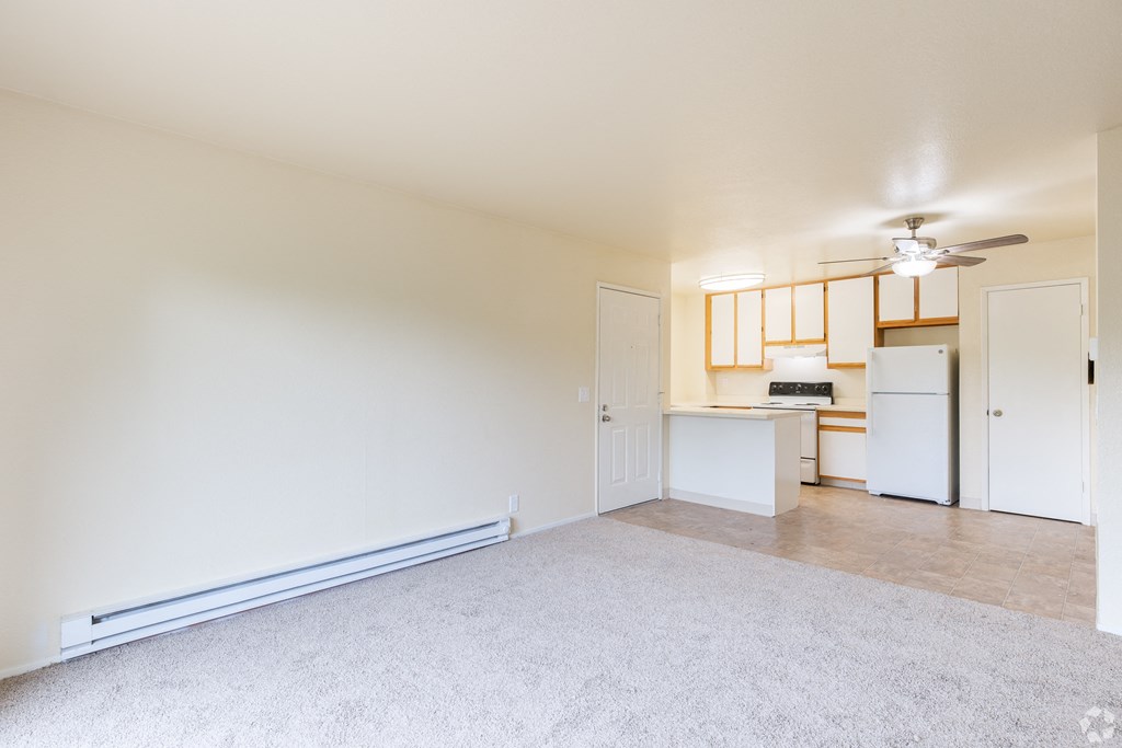 an empty living room with a kitchen and a ceiling fan