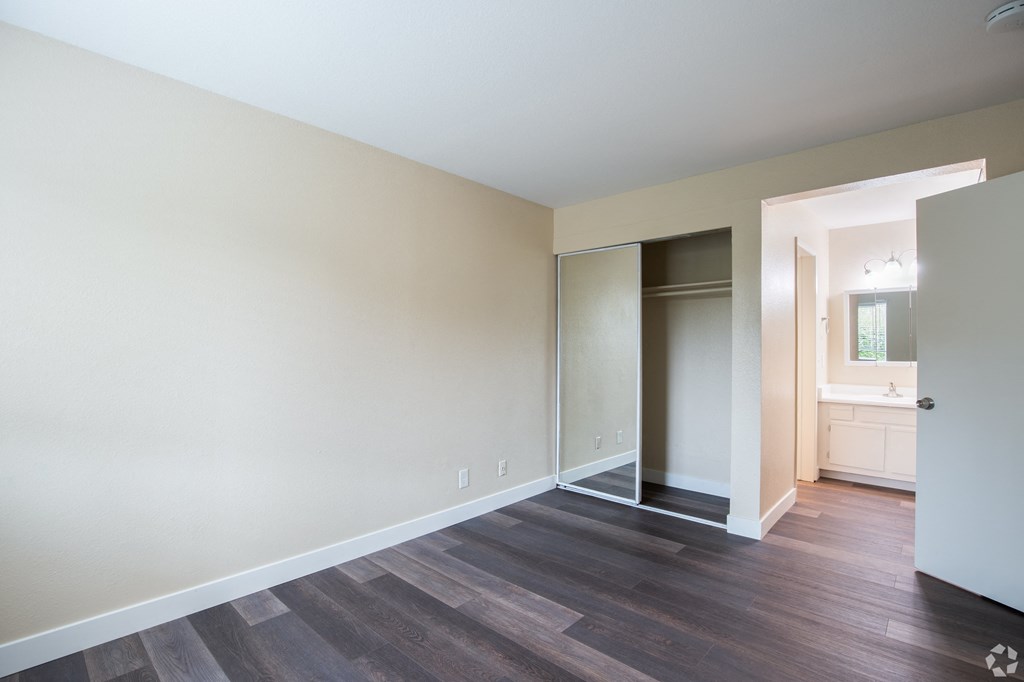 an empty living room with hard wood flooring and a glass door to a bathroom