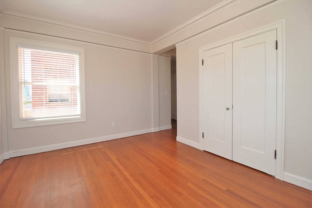a bedroom with white walls and wood floors and a window