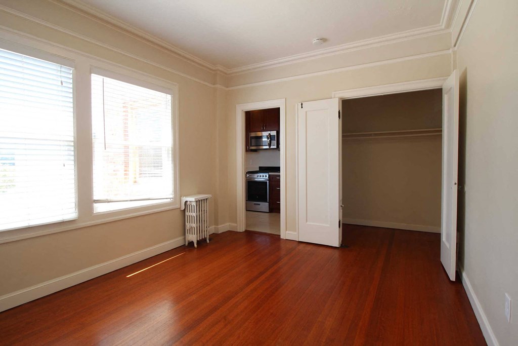 an empty living room with wood floors and a door to a kitchen