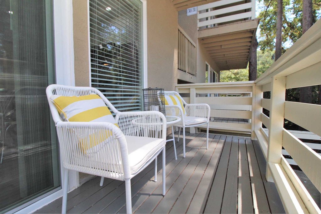 a porch with white wicker chairs and a yellow and white pillow