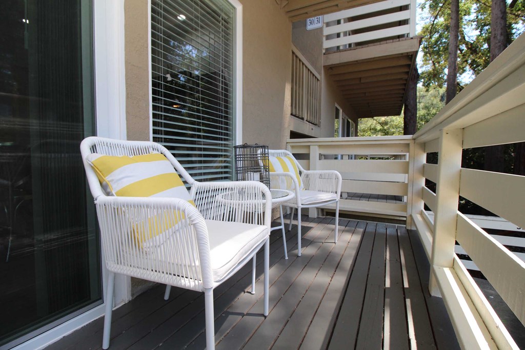 a porch with white chairs and a yellow and white pillow