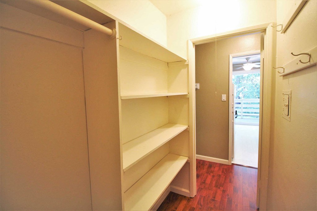 a walk in closet with empty shelves and a door to a room
