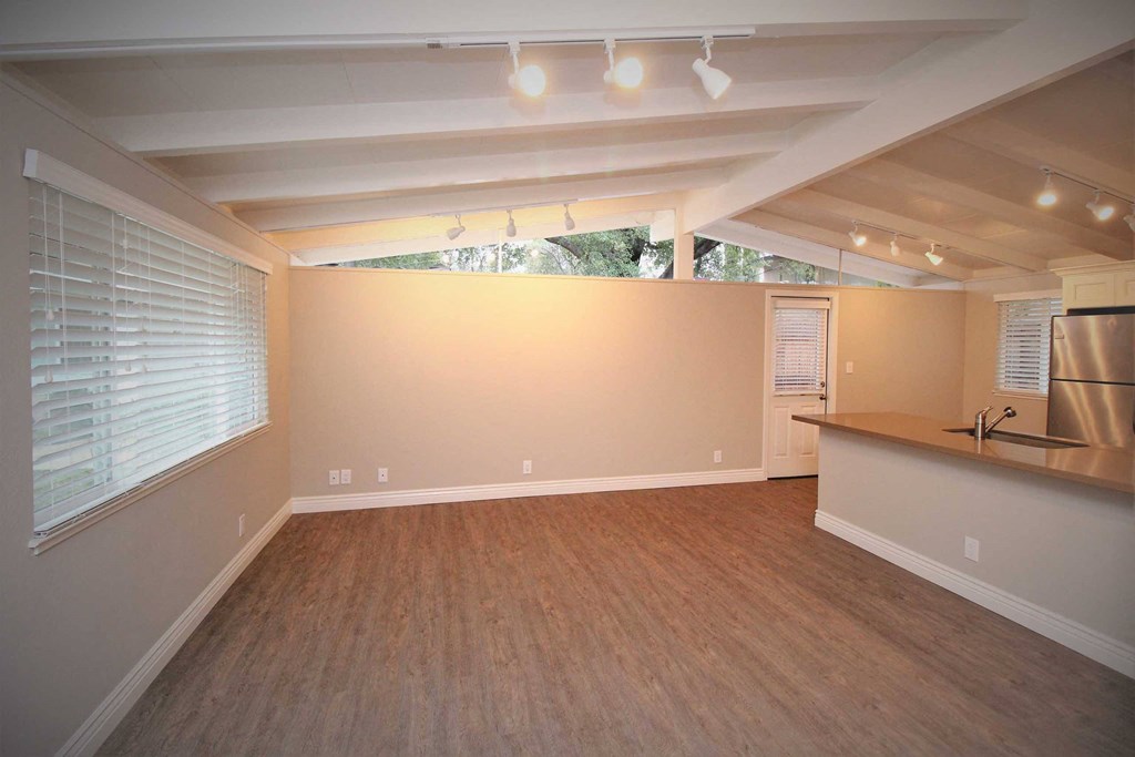 an empty living room with a kitchen and a large window