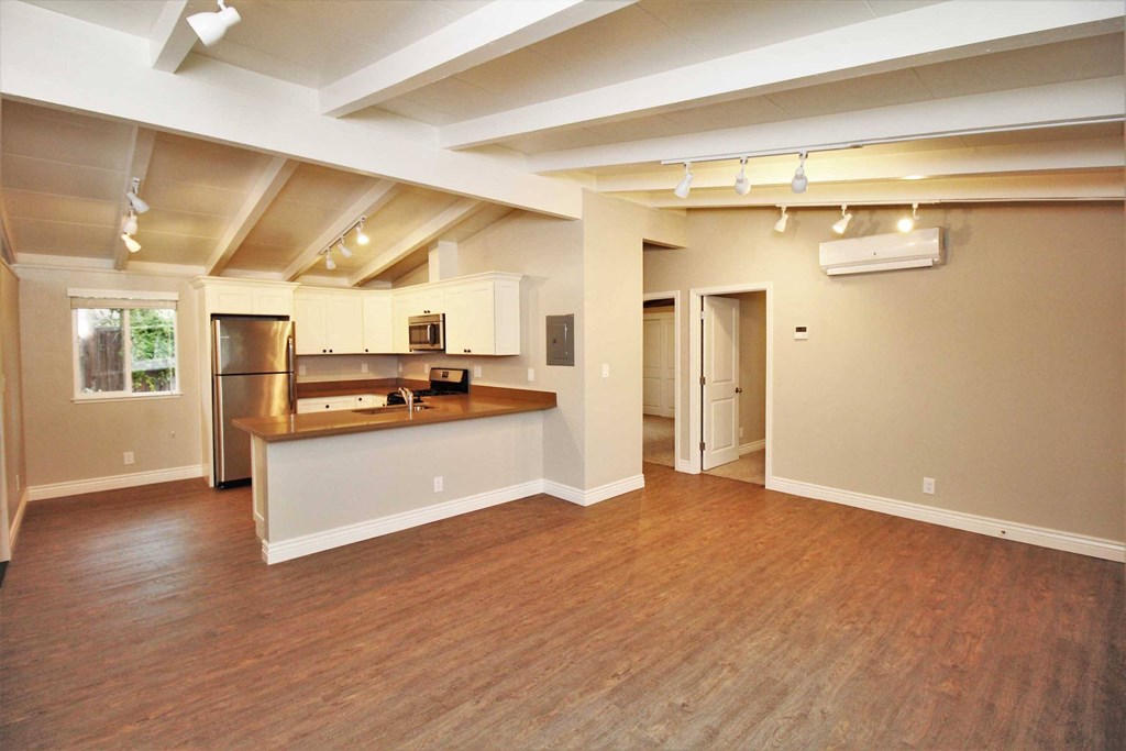 an empty living room with a kitchen and a hard wood floor