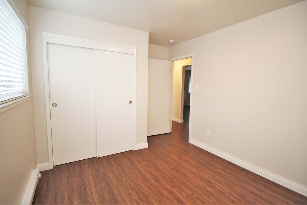 a bedroom with white walls and wood flooring and a closet