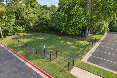 A parking lot with a green grass area and a fence.