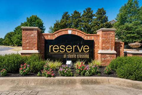 A sign that says "reserve at steele crossing" is in front of a brick wall.