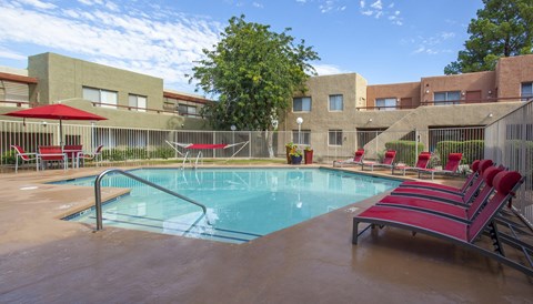 A pool with red chairs and a building in the background.