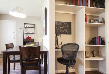 A dining room with a table and chairs and a shelf with books and a chalkboard.