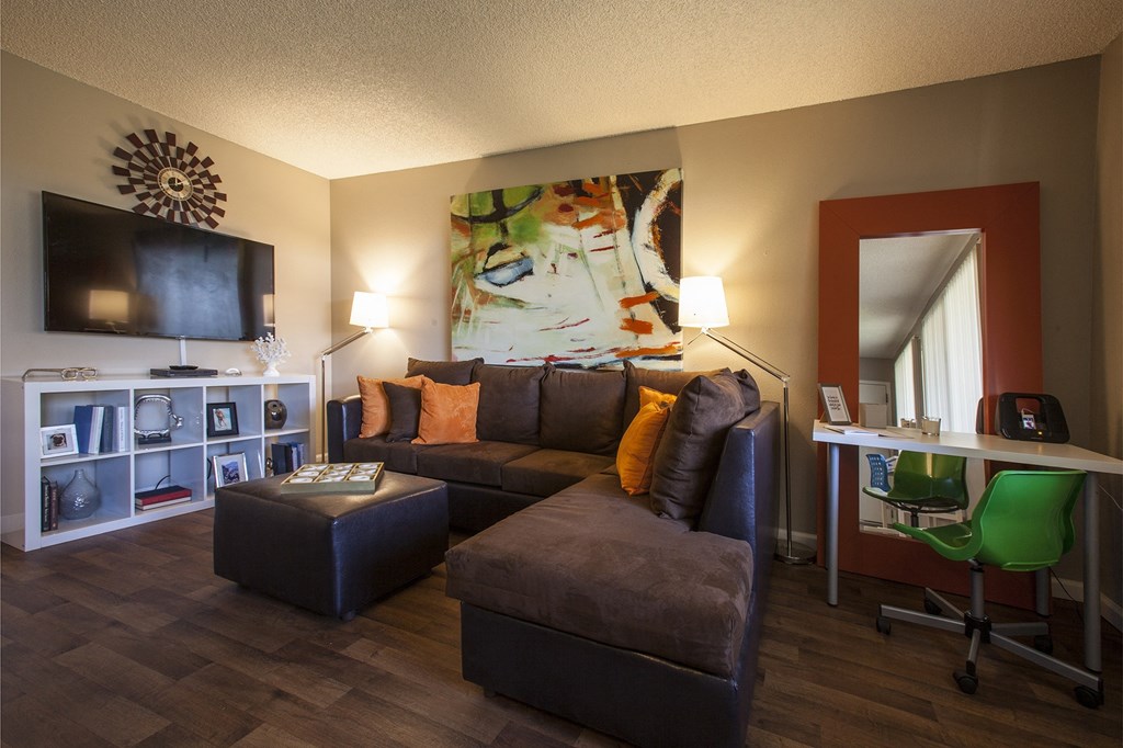 A living room with a brown couch, a white desk, and a green chair.