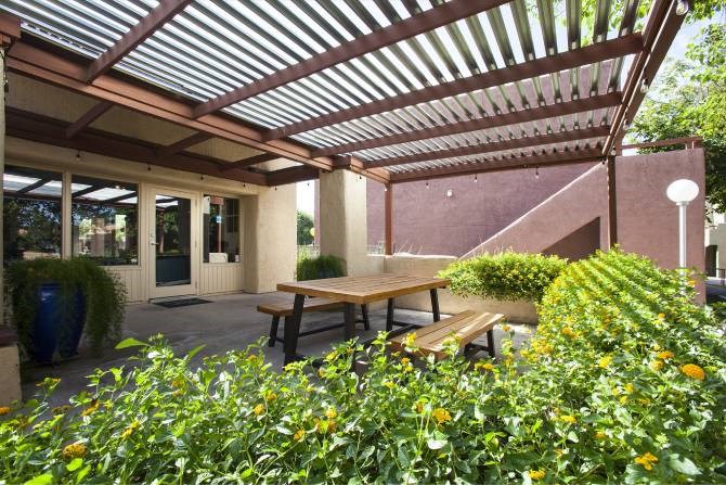 A patio with a wooden table surrounded by green plants.