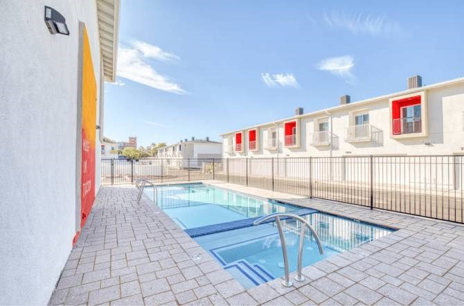 A swimming pool with a metal fence and a building with red windows in the background.
