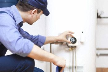 A man in a blue shirt and cap is fixing a water heater.