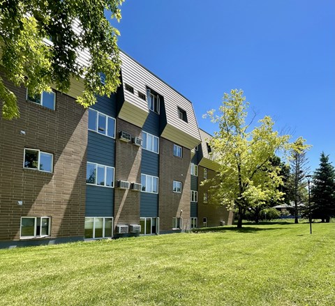 a brick apartment building with green grass and trees