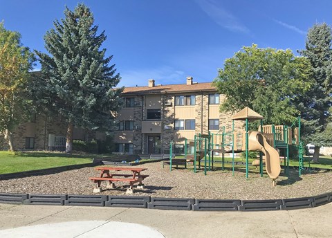 A playground with a slide, picnic table, and a building in the background.