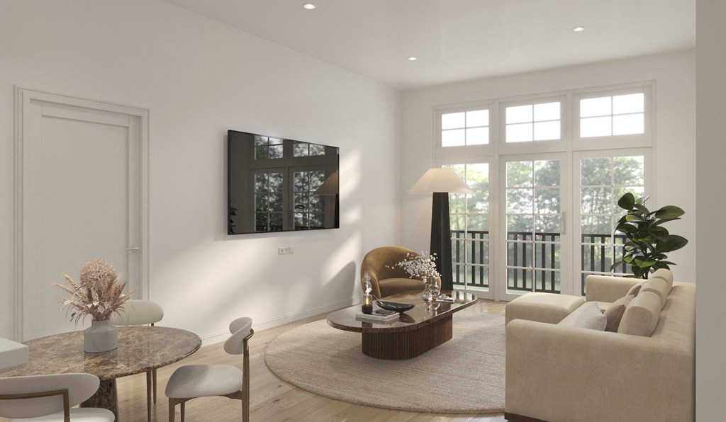 A modern living room with a white sofa, a round table, and a flat-screen TV mounted on the wall.