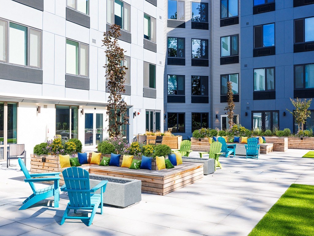 an outdoor patio with blue chairs and benches in front of an apartment building