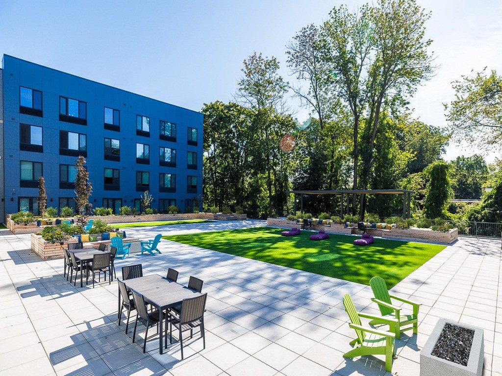 a patio with tables and chairs next to a lawn and a blue building