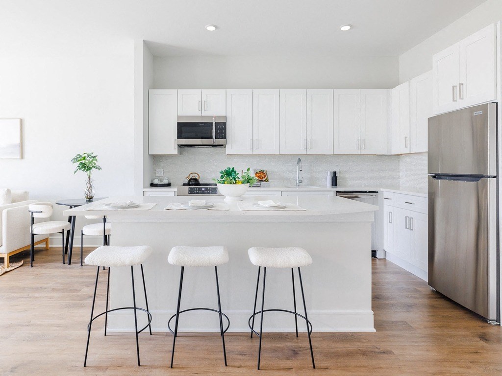 a kitchen with white cabinets and a large island with three stools