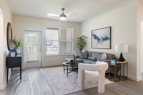 A living room with a grey couch, a white chair, and a painting on the wall.