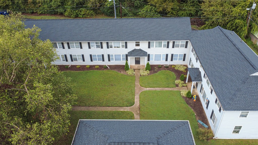 A white building with a black roof is surrounded by a green lawn.