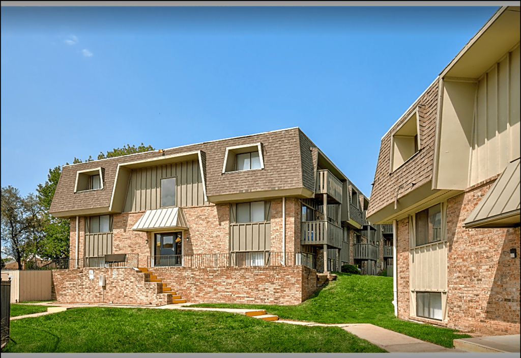 an apartment building with a grassy yard and a blue sky