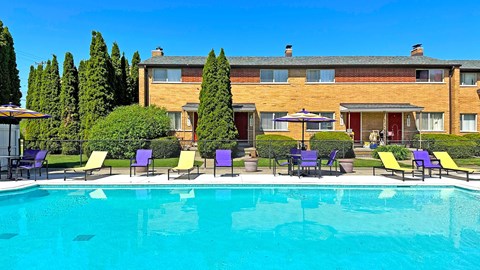 A swimming pool in front of a building with chairs around it.