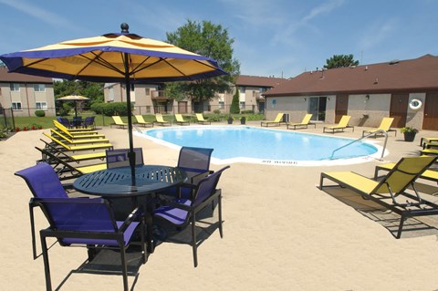 A pool with chairs and an umbrella in the foreground.