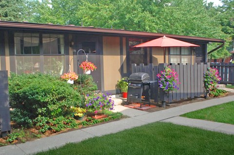 A house with a brown and tan exterior has a red umbrella on the patio.