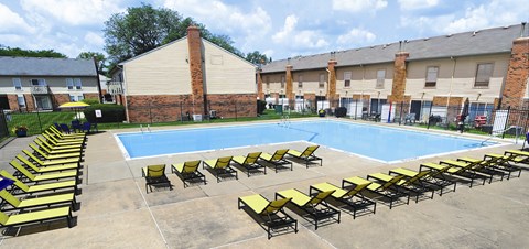 A pool surrounded by sun loungers and a brick building.