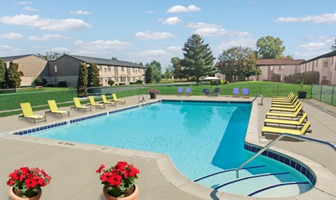 A swimming pool surrounded by yellow lounge chairs and red flowers.