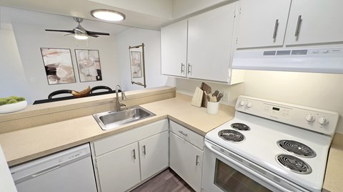 A white kitchen with a stove, sink, and cabinets.