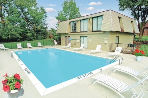 A pool with chairs and a house in the background.