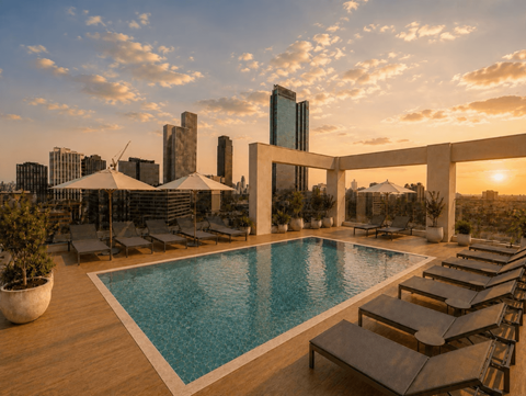 A rooftop pool with lounge chairs and a city skyline at sunset.
