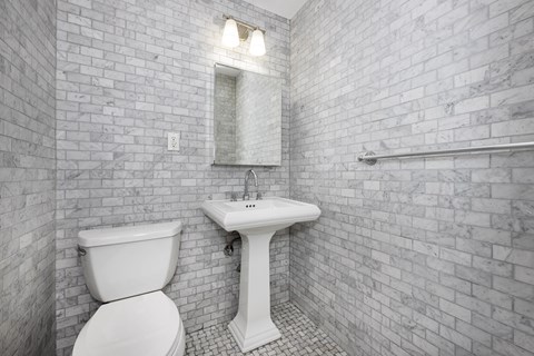 A white toilet and sink in a bathroom with a brick wall.