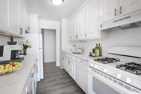 A white kitchen with a stove and a bowl of fruit on the counter.